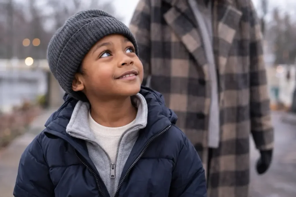 Boy wearing a thermal top, gray fleece and navy winter jacket with a knitted beanie.