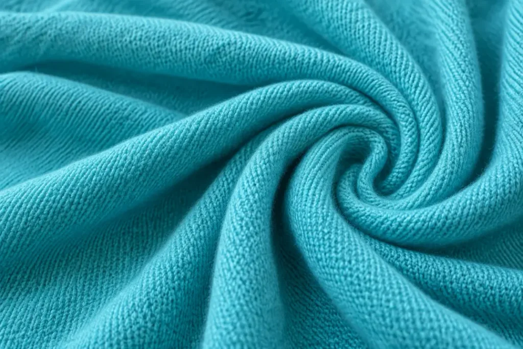Close-up of turquoise knitted fabric arranged in soft folds, showing its surface texture.